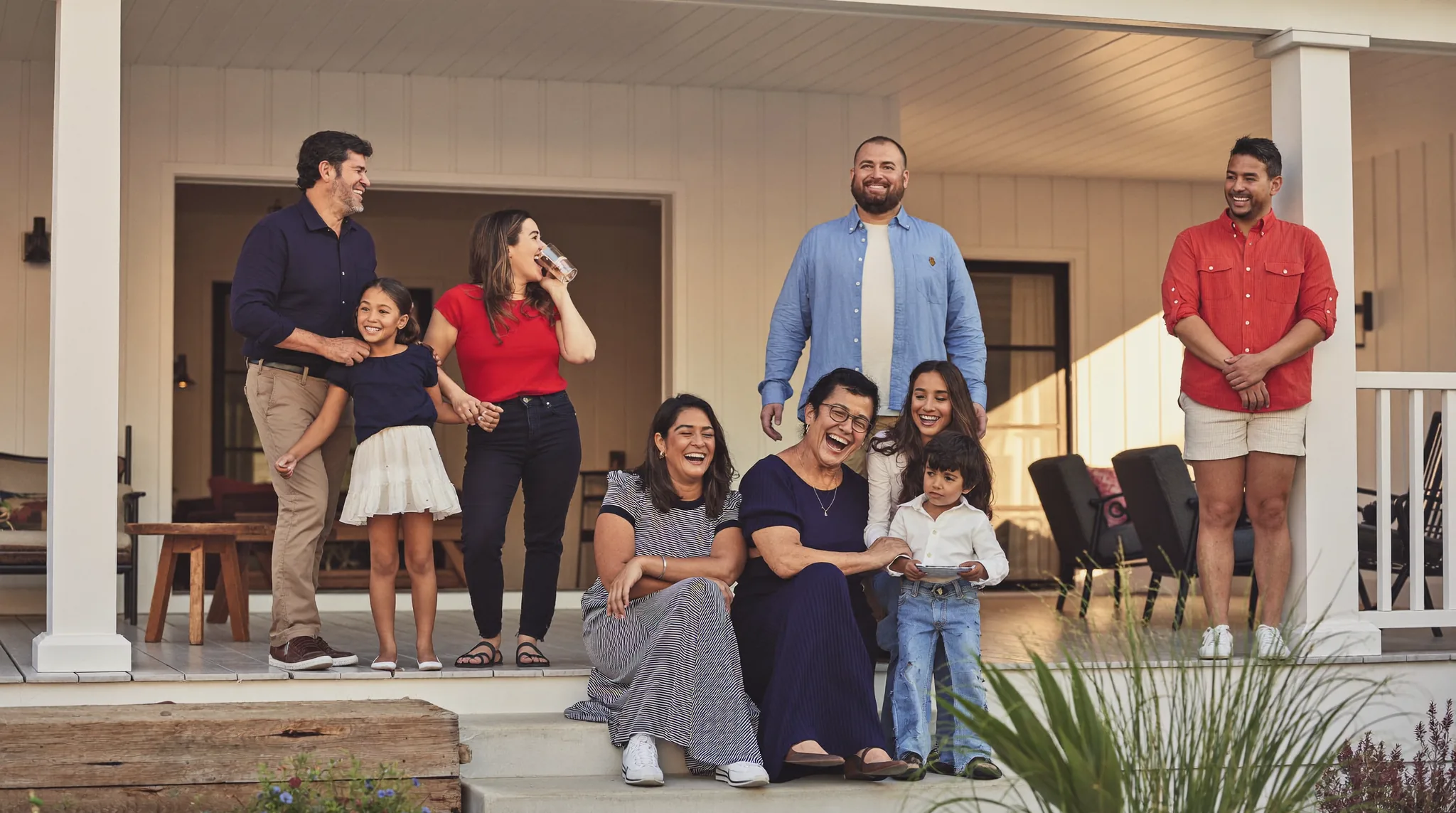 A multigenerational family gathered on a wide Southern front porch at golden hour