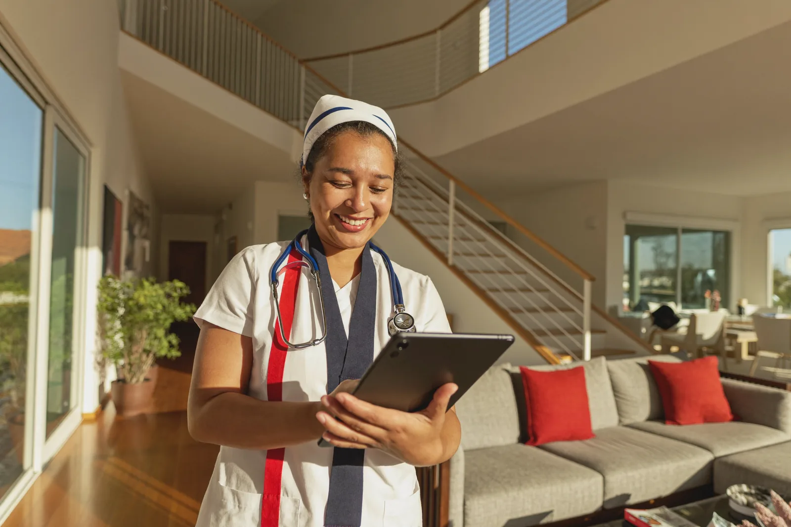 A nurse with a stethoscope and tablet smiling in a bright senior community lounge