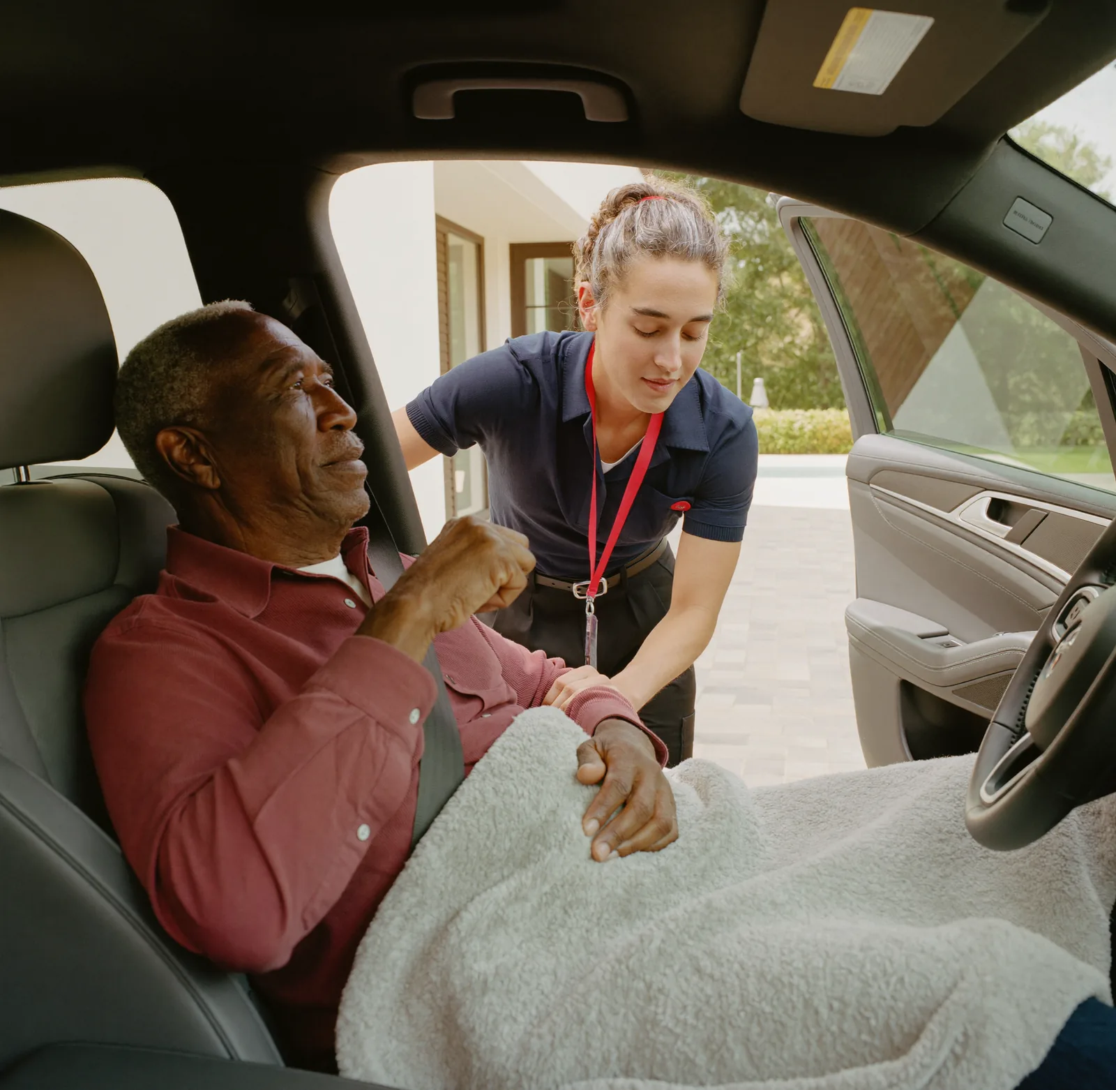 A caregiver gently helping a senior man into the passenger seat of a car