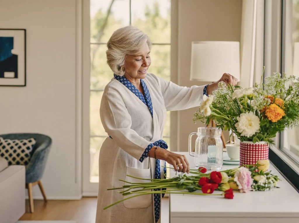 A senior arranging fresh flowers at a sunlit dresser in the morning