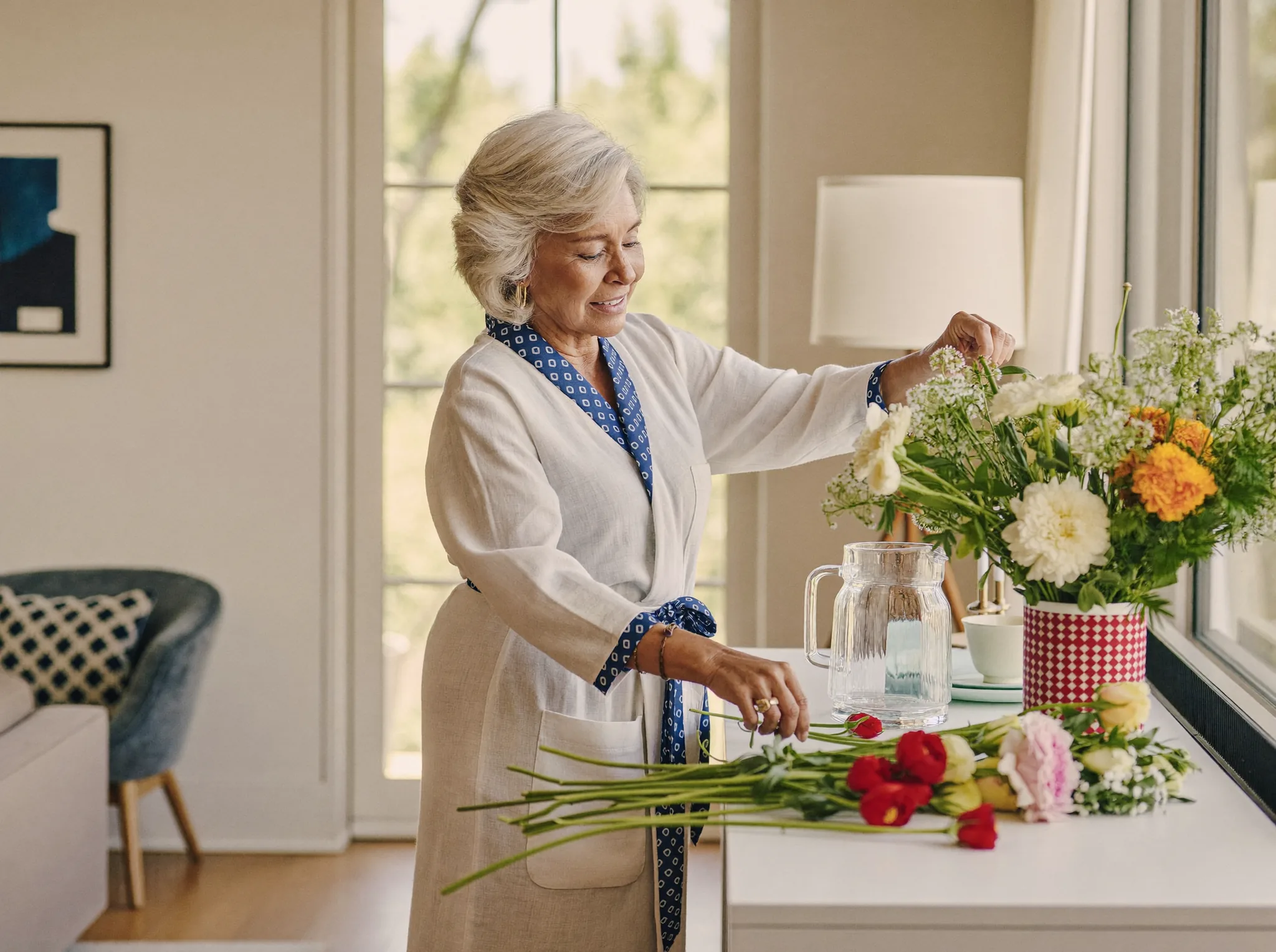 A senior arranging fresh flowers at a sunlit dresser in the morning
