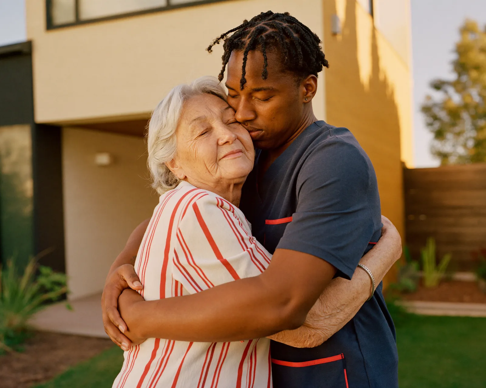 A senior woman warmly embracing her caregiver outdoors in a sunny garden