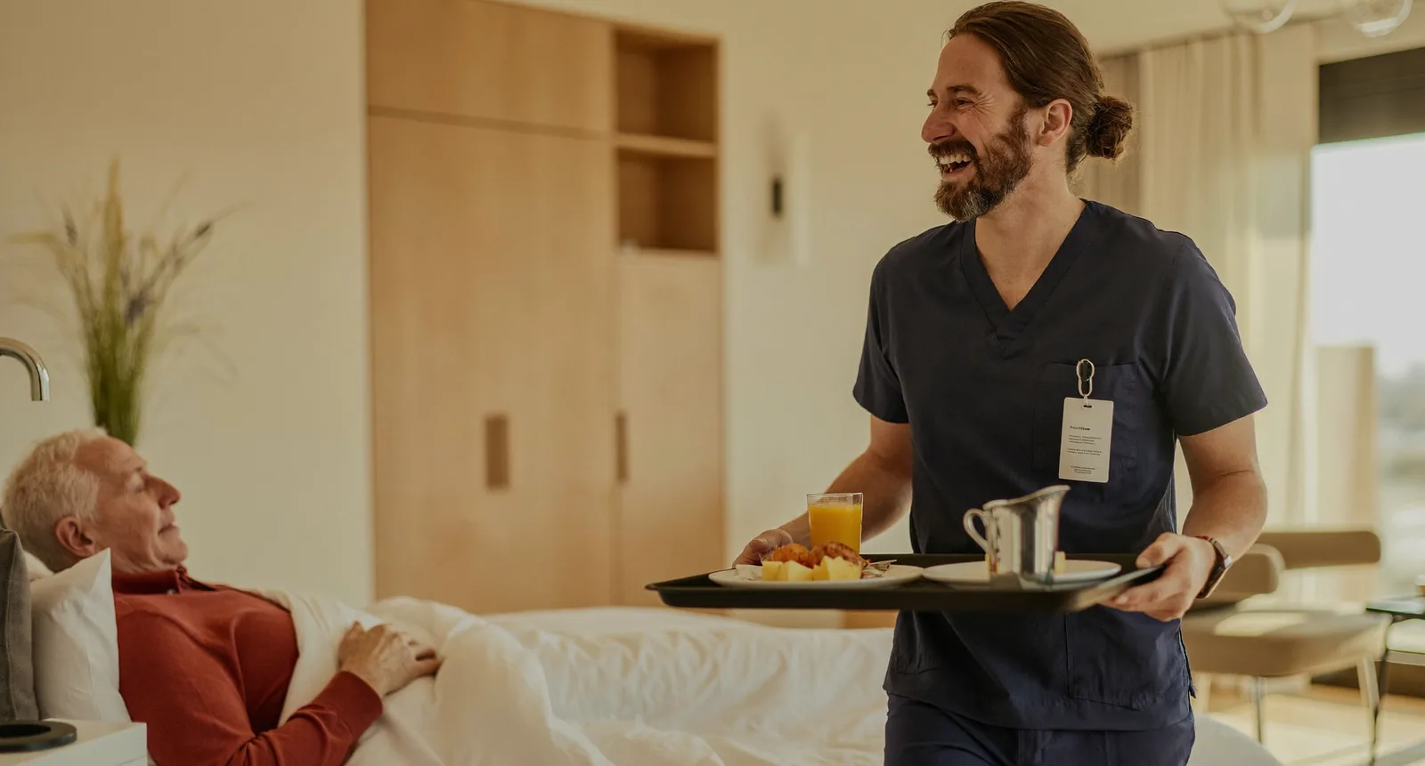 A caregiver bringing a breakfast tray to a senior resting in a softly lit bedroom