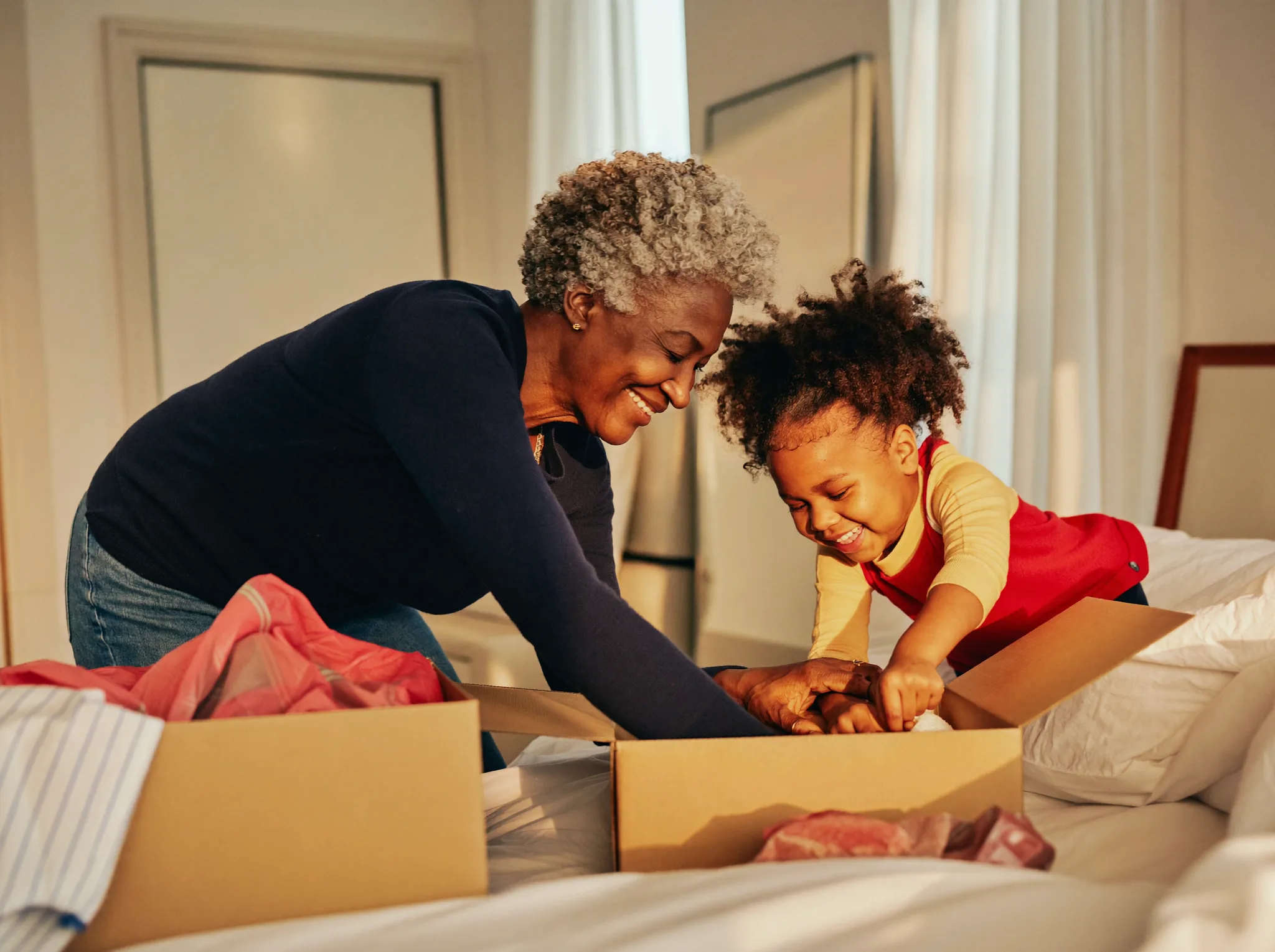 A senior and her adult daughter unpacking a moving box in a warmly lit bedroom